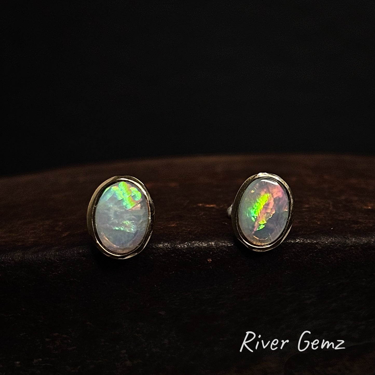 Green and orange crystal opals set in yellow gold stud earrings against a dark background with 'River Gemz' branding.
