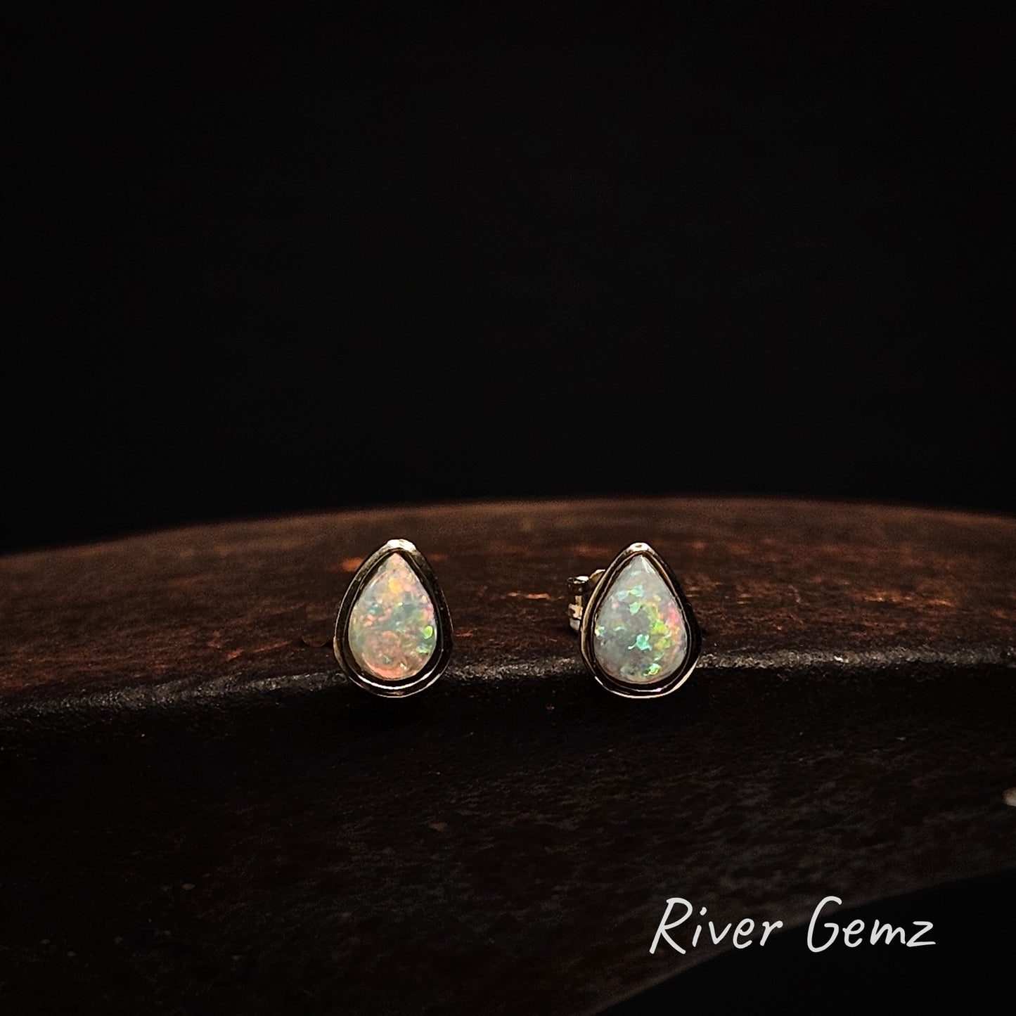 Tear drop shaped multi-coloured light opals set in yellow gold stud earrings.