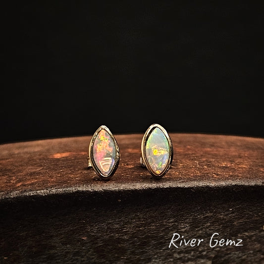 Multi-coloured crystal opals in gold earrings on a cast iron shoe anvil with 'River Gemz' branding.