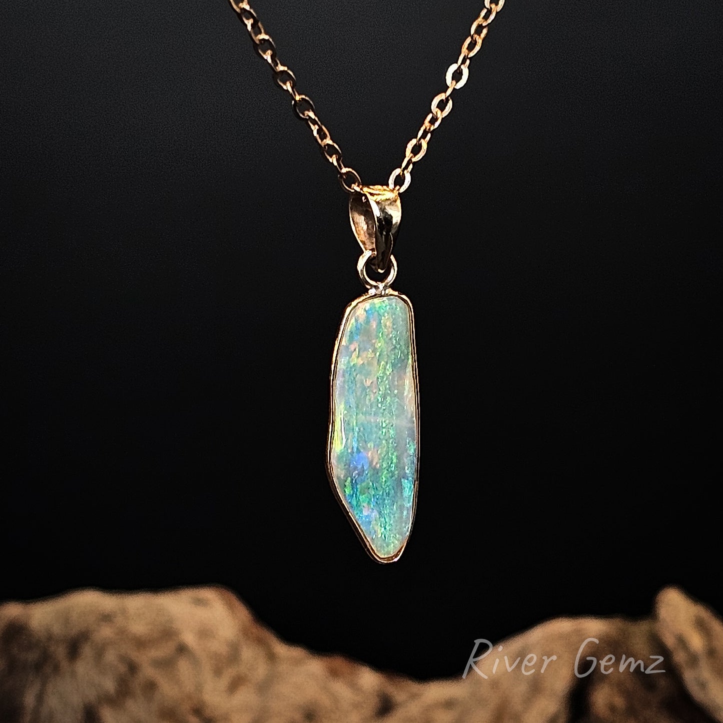 Crystal opal set in 14K yellow gold pendant against a dark background with 'River Gemz' branding.