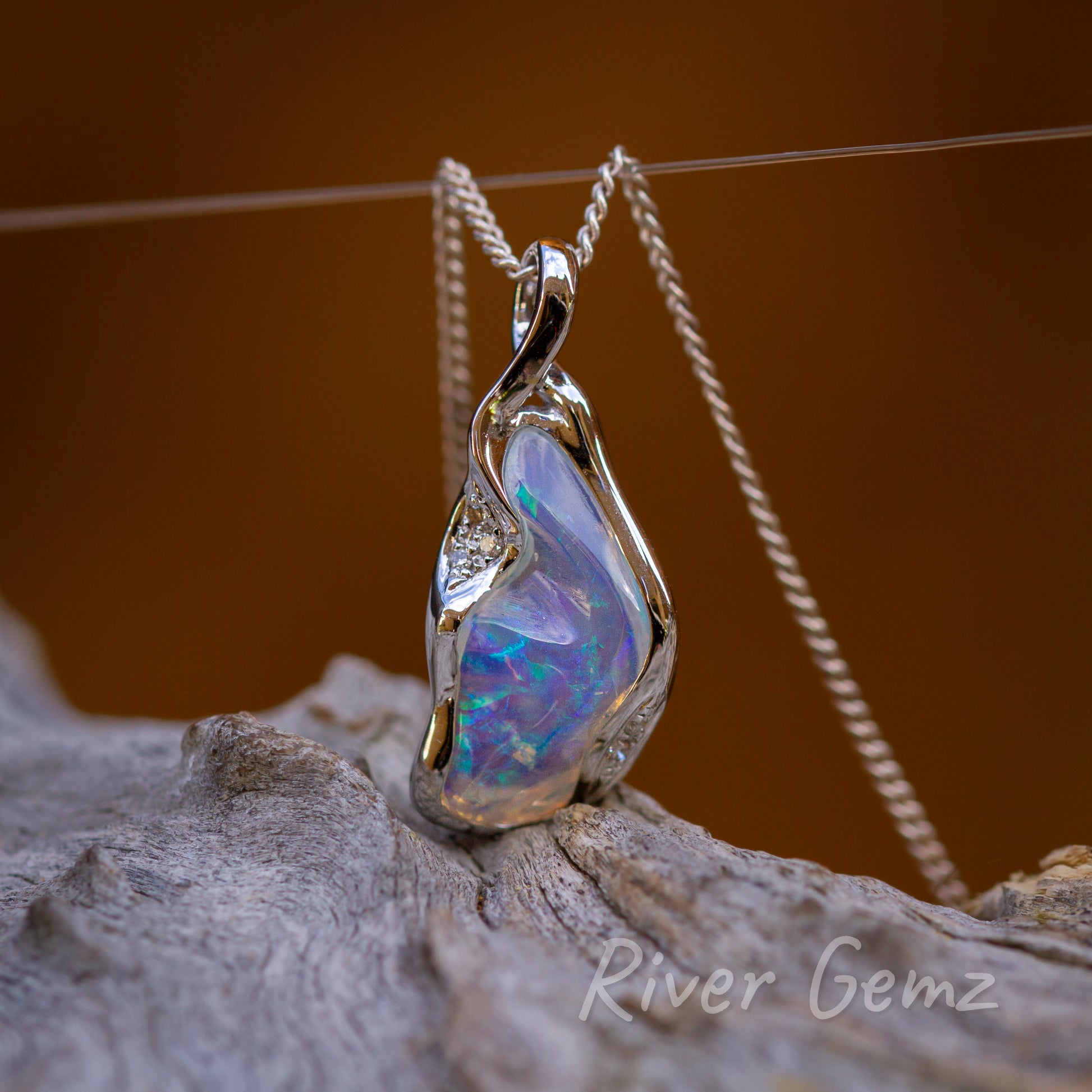 Free form cut opal besel set in white gold with chain passing through an integrated loop of the pendant design.