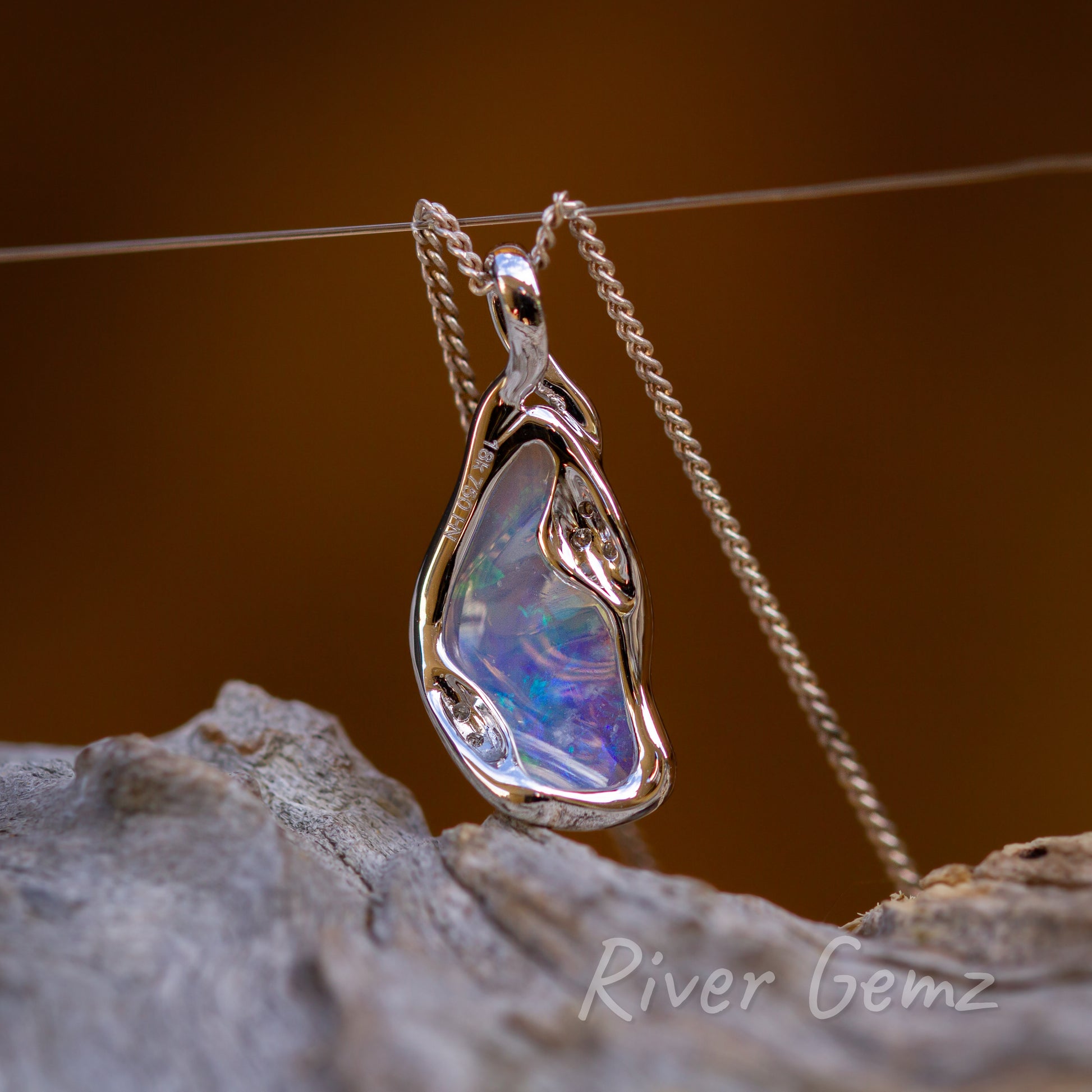 The reverse side of the necklace shows the hall mark of the gold setting and the transparency of the crystal opal. All 3 photos have a burnt orange background with the pendant base sitting above a weathered grey bit of drift wood.