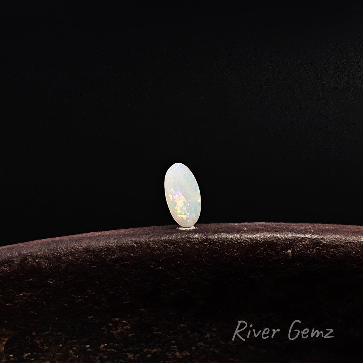 Slightly side on view of oval shaped white opal on a rusty shoe anvil and black background.