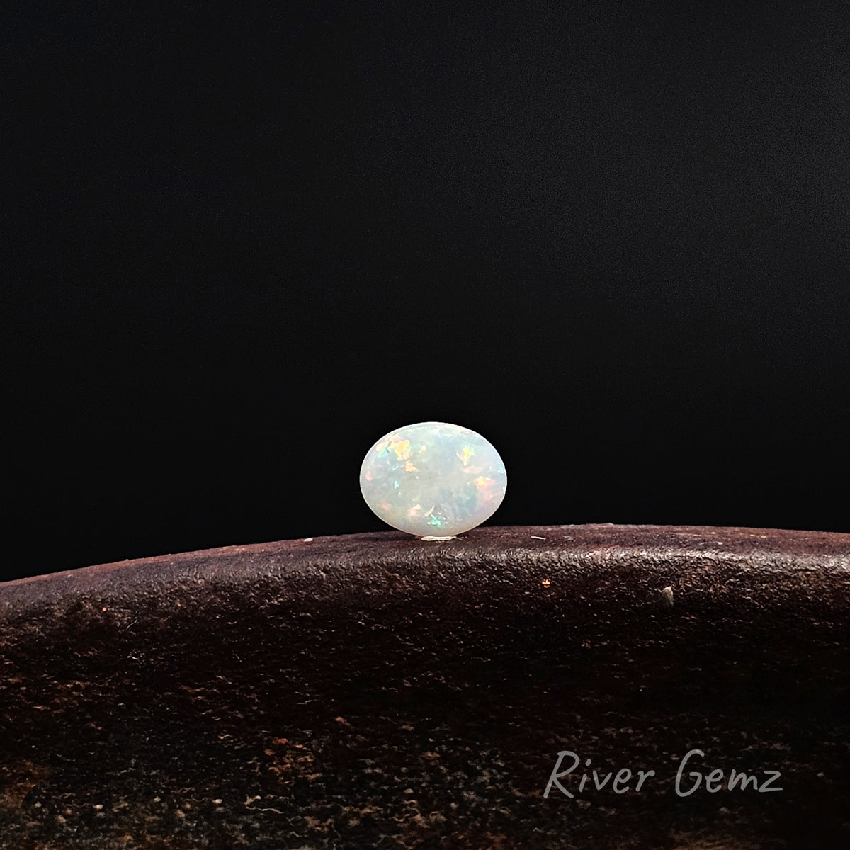 Oval shaped white opal lying horizontally on a brown surface and black background.