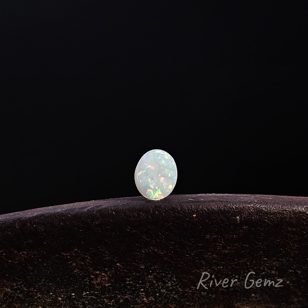 Multi-coloured light opal on a brown surface.