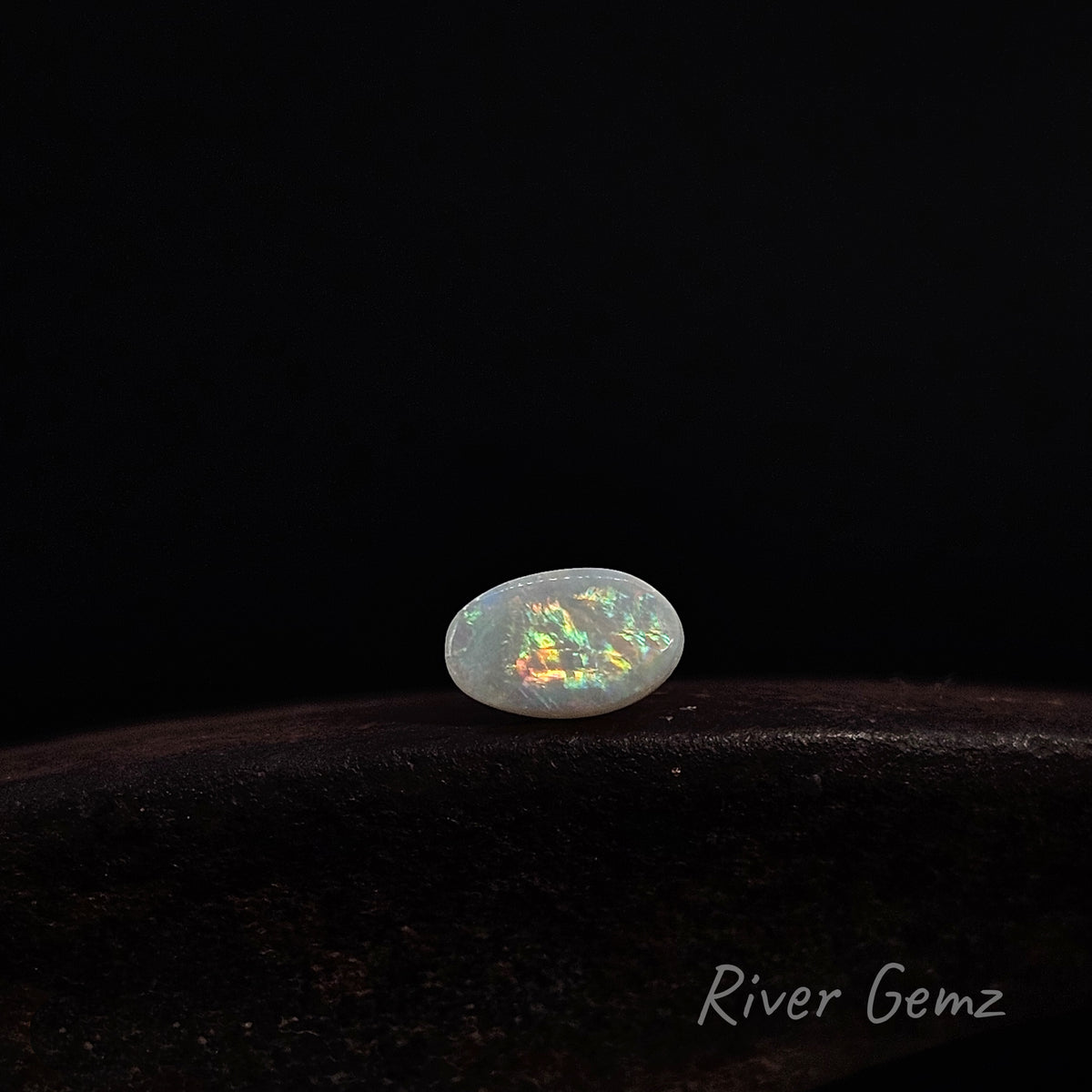 Light opal loose shown lying in an East-West orientation on a dark brown surface.