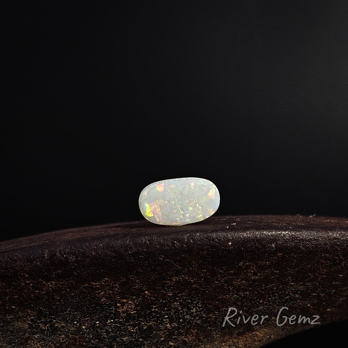 Multi-coloured white opal lying horizontally on a shoe anvil against a dark background.