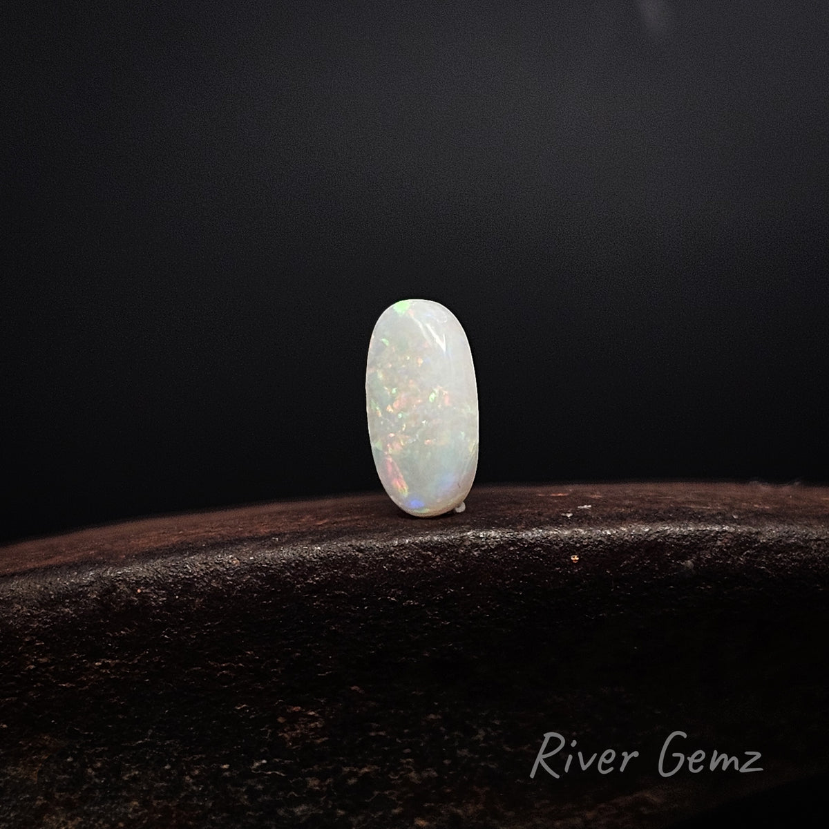 Slightly side on view of white opal cut in an oval shape on a brown surface and black background.