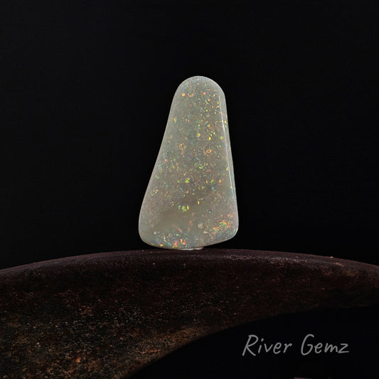 Multi-coloured free-form cut light opal on a shoe anvil against a black background and 'River Gemz' watermark in the bottom right hand corner.