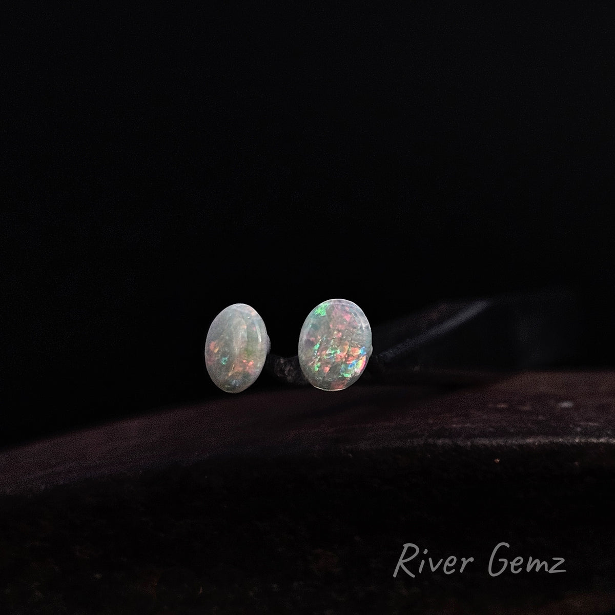 Colourful light opals cut to an oval shape on a dark background.