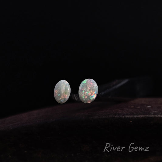Colourful light opals cut to an oval shape on a dark background.