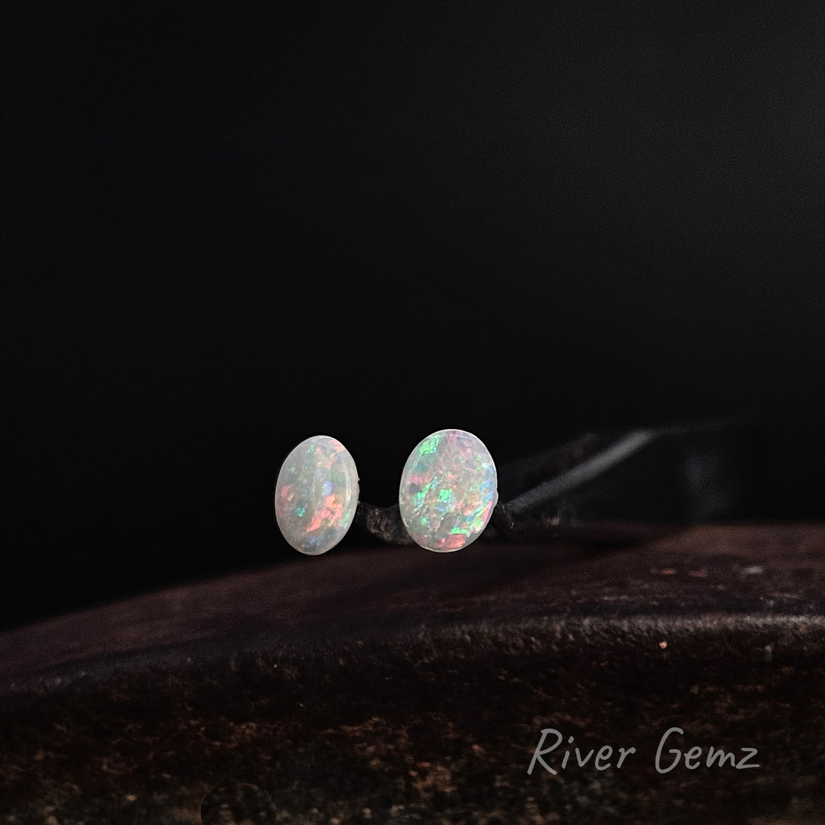 Multi-coloured oval shaped pair of loose opals shown against a black background and 'River Gemz' watermark in the the bottom right hand corner.