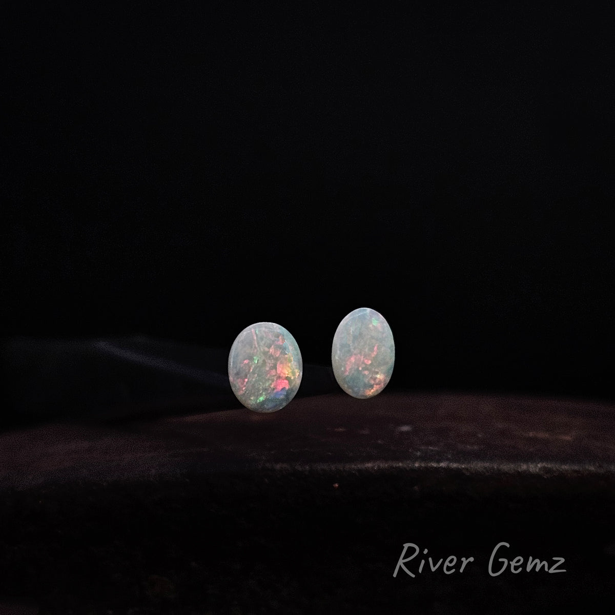 Pair of unset multi-coloured white opals against a black background.