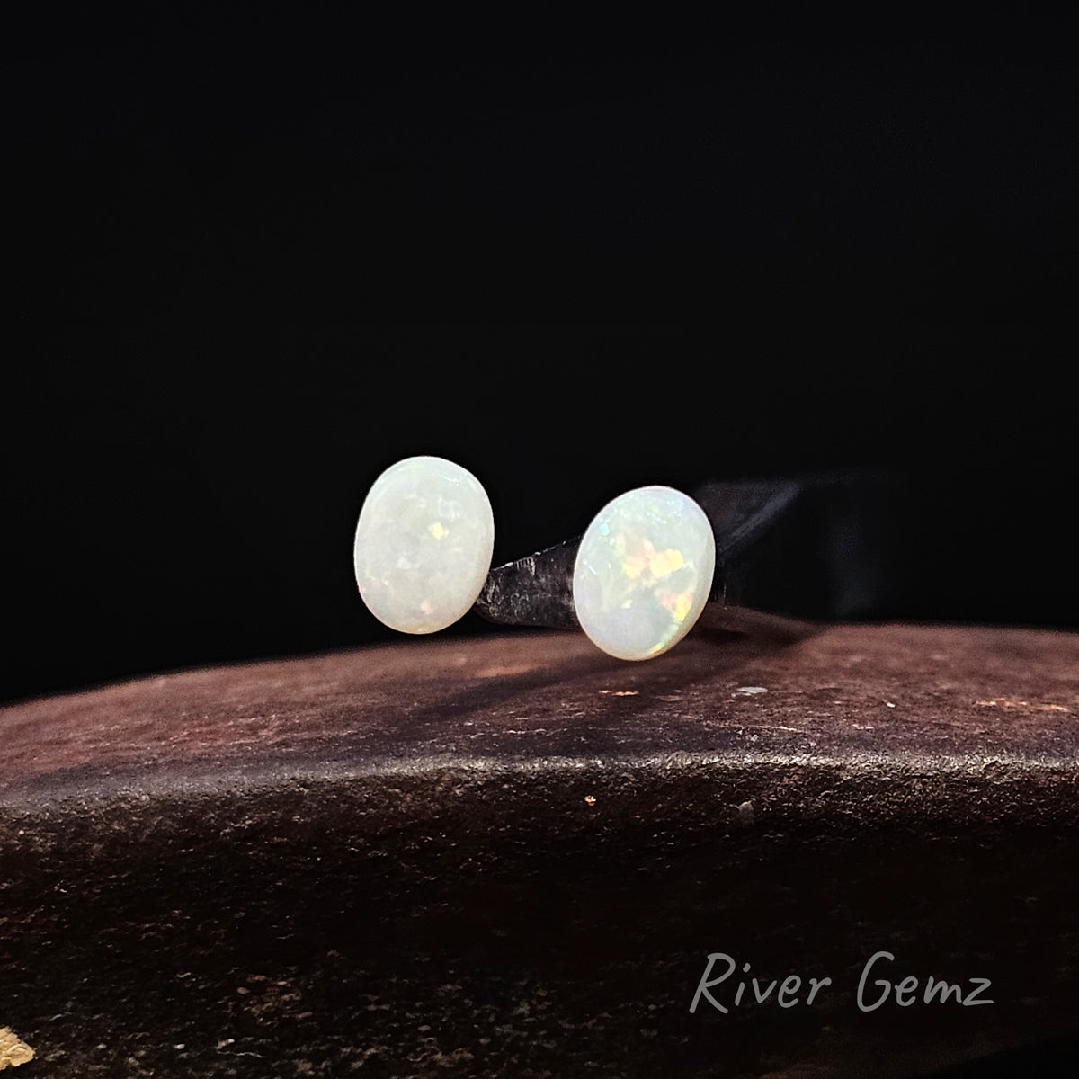 Pair of unset oval shaped multi-coloured white opals against a black background and 'River Gemz' watermark in the bottom right hand corner.