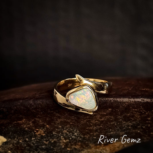 Gold ring with a triangular shaped light opal on a dark background, branded 'River Gemz'.