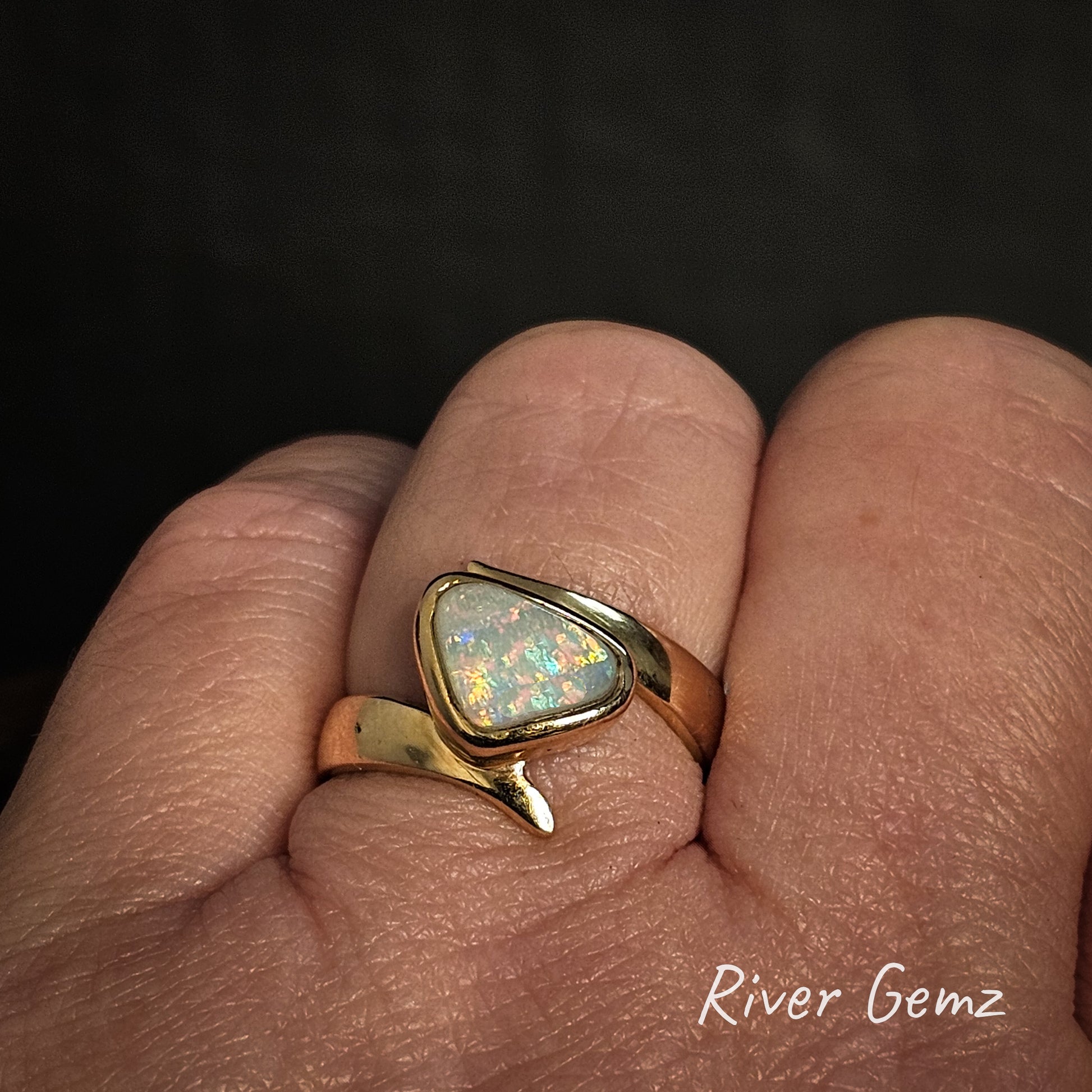 Gold ring with an opal stone on a finger, branded 'River Gemz'.