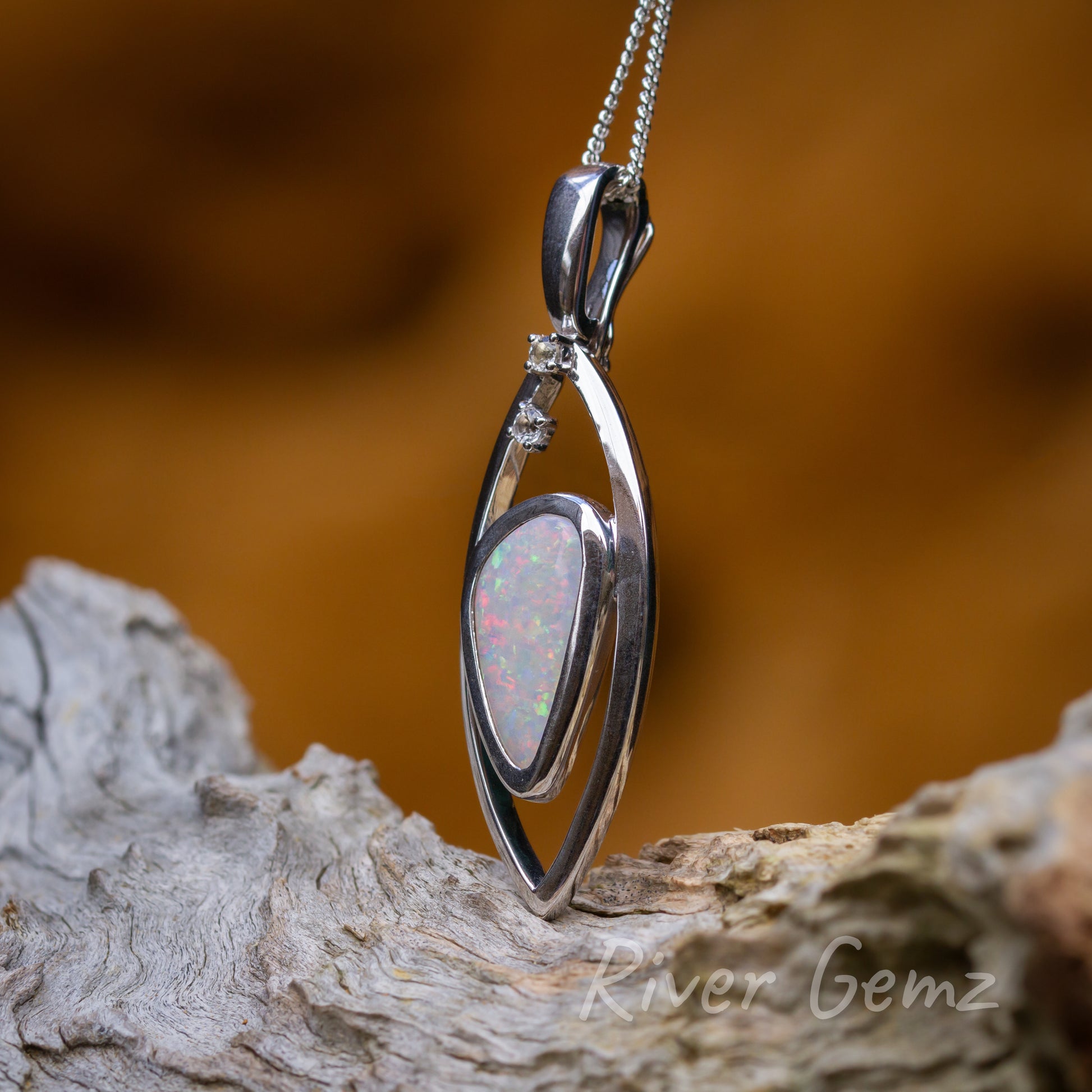 Triangular shaped opal besel set and sitting within a gridiron ball shaped setting. Two topaz stones claw set at the peak of the pendant.