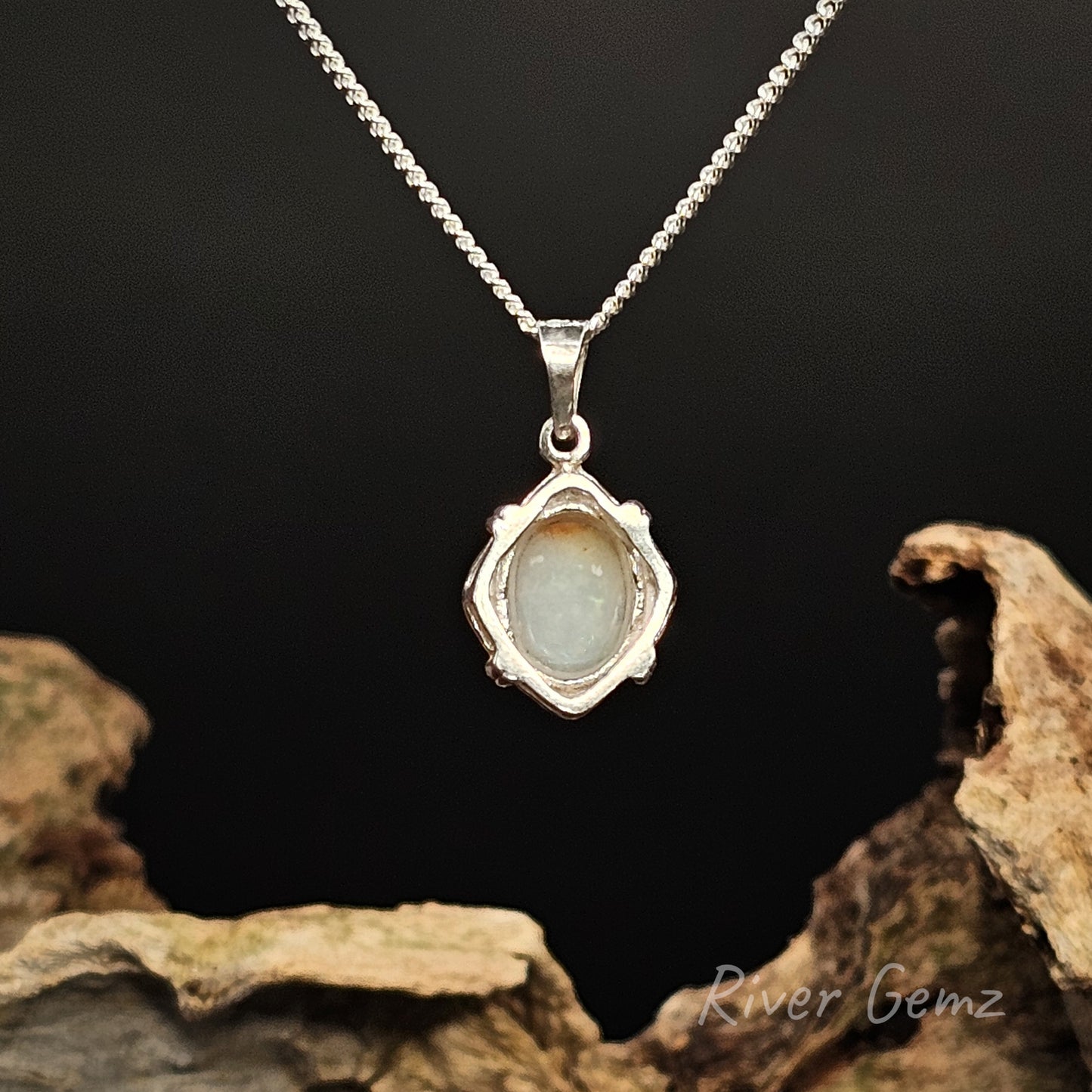 Back of the silver pendant shows the light base tone of the white opal set in it on a dark background