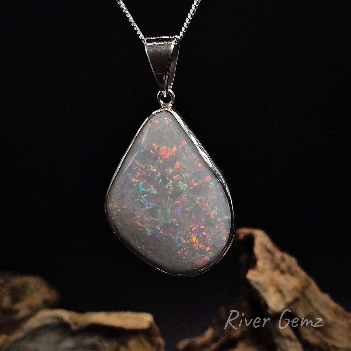 Colourful light opal besel set in sterling silver pendant against a black background.