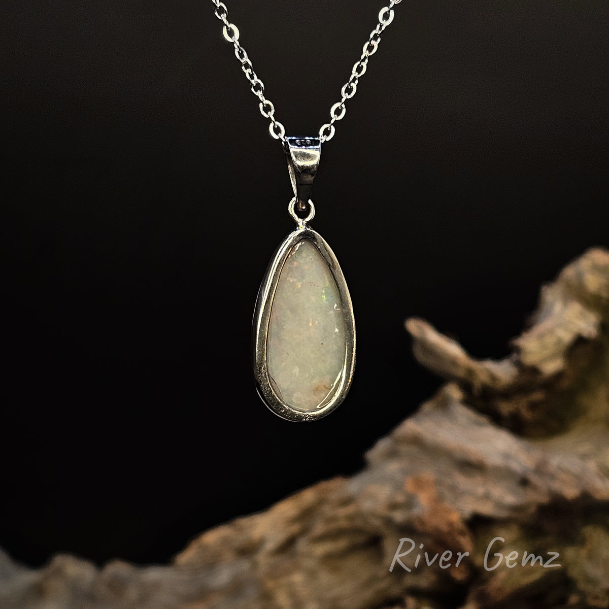 Rear view of  necklace shows the light base tone of the white opal, displayed on a dark background with a piece of driftwood and a 'River Gemz' watermark.