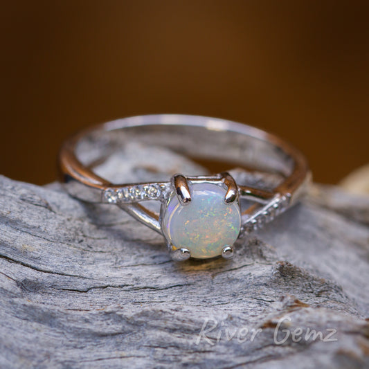 Circular multi-coloured light opal set in a silver ring with a line of white topaz each side of the opal.