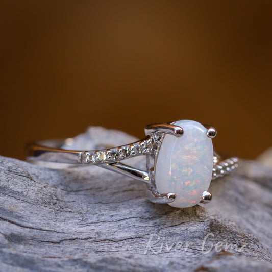 Light opal in silver ring sitting on light grey grained wood and burnt orange back drop.