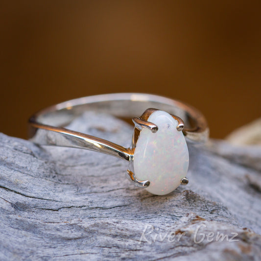 Tear drop shaped white opal in silver ring resting on light grey grained wood.