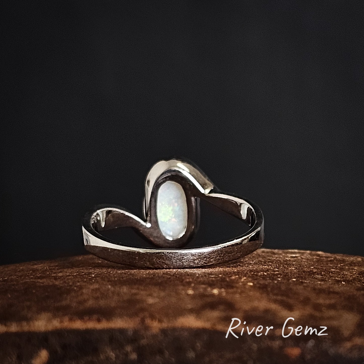 Rear view of silver ring with a central white opal on a dark background, branded 'River Gemz'.