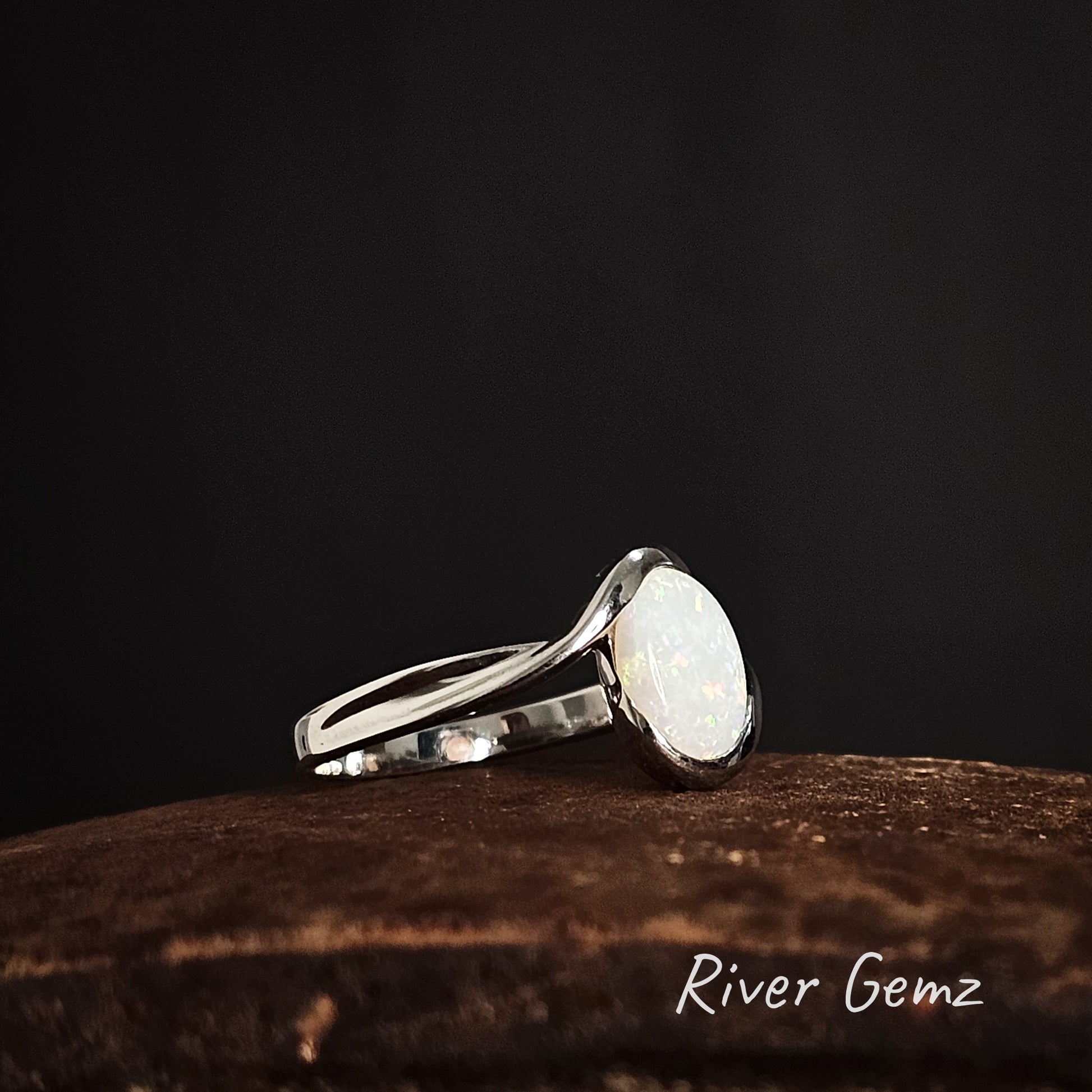 Side view of silver ring with a white opal on a dark background, branded 'River Gemz'.