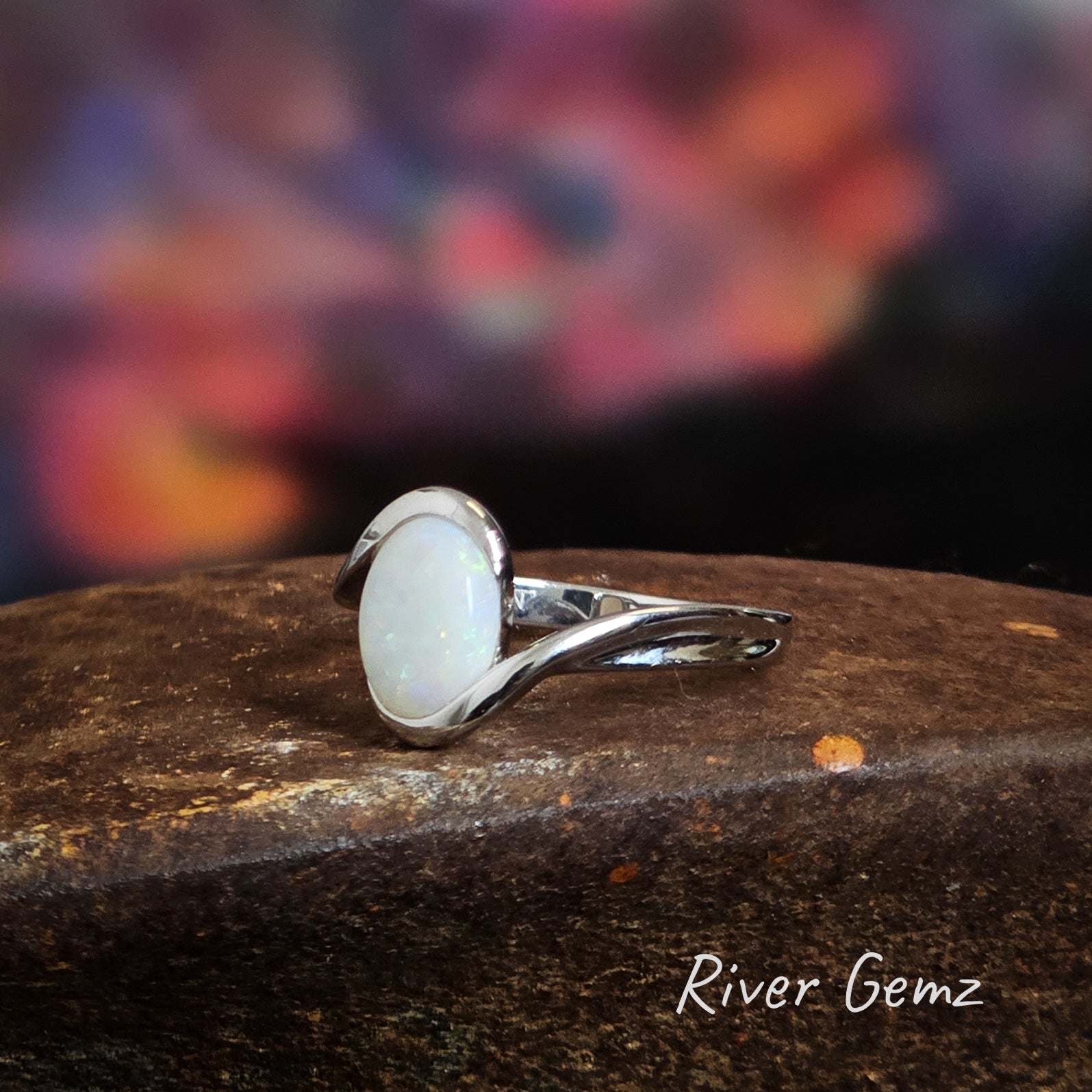 White opal with flecks of colour set in a sterling silver ring with an ocean wave type of design.