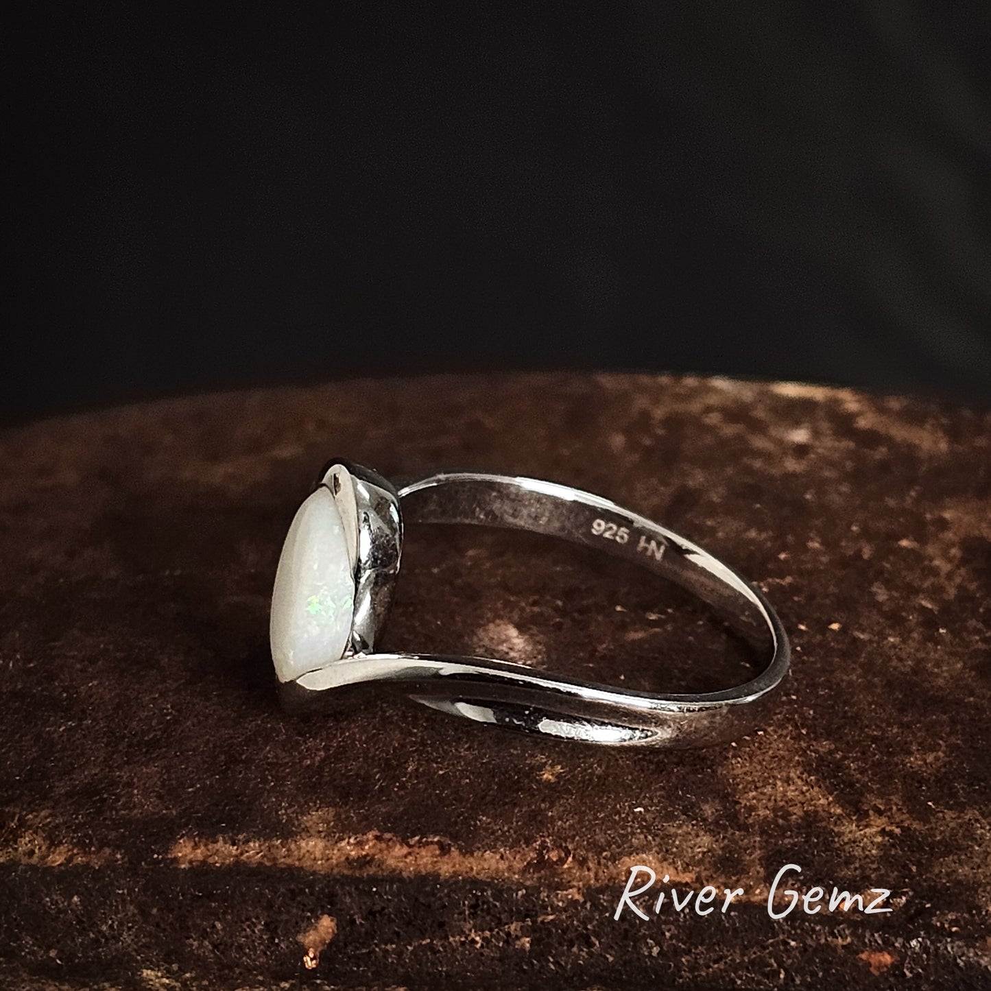 Side view of ring showing the 925 mark for sterling silver with a white stone on a dark brown surface, branded 'River Gemz'.
