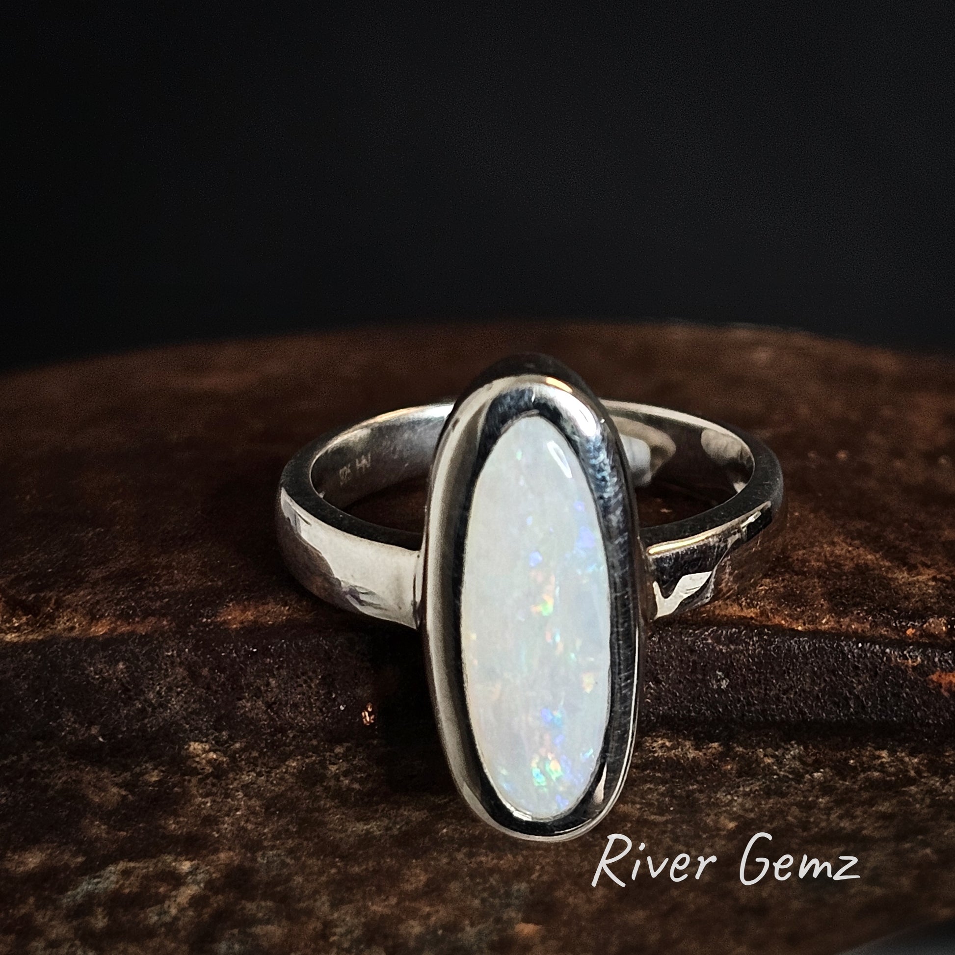 Silver ring with a white opal stone on a dark background, branded 'River Gemz'.