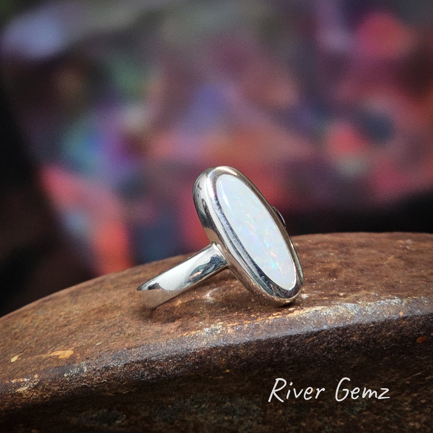 Oval shaped white opal with flicks of multiple colours set in sterling silver ring.