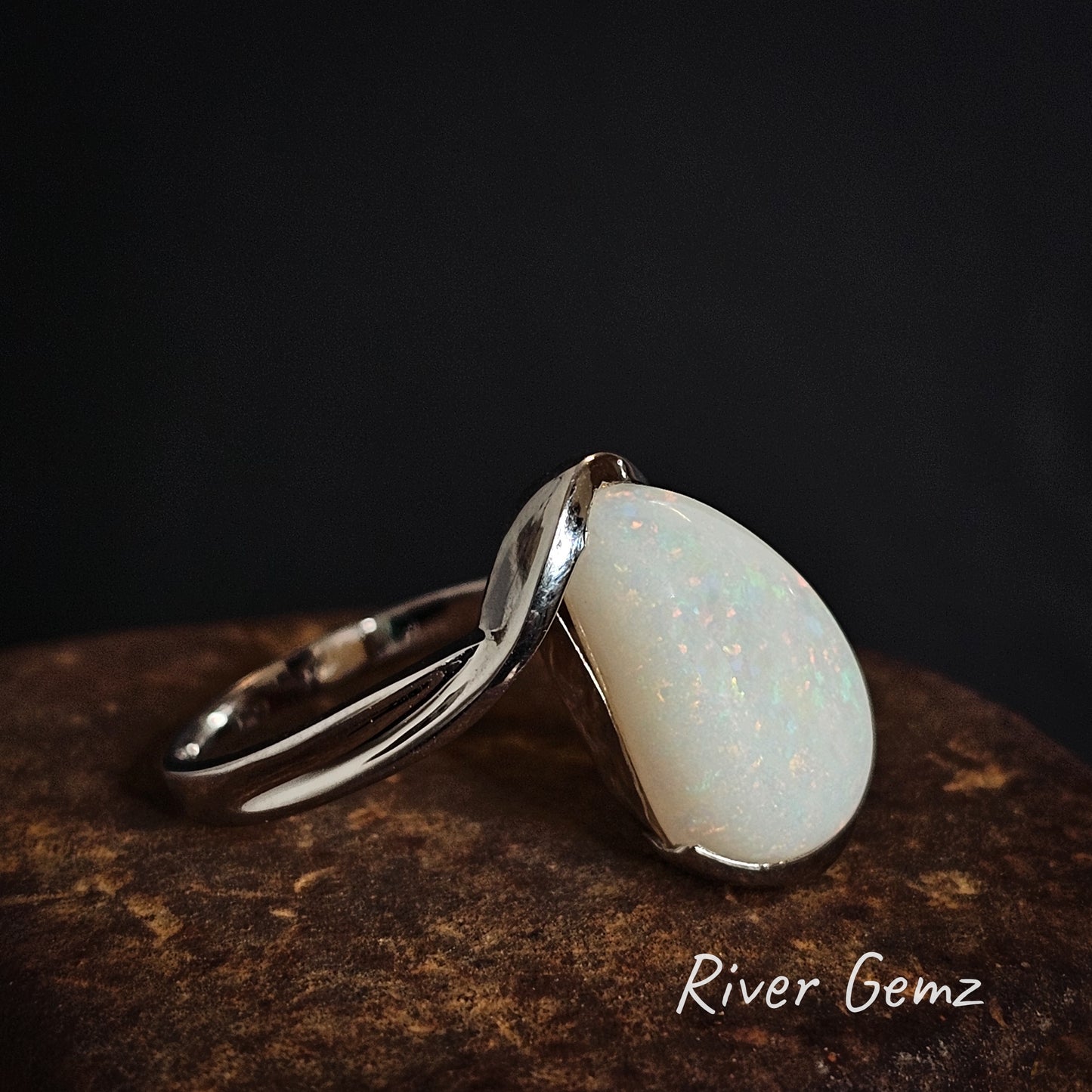 Silver ring with a white opal stone on a dark background, branded 'River Gemz'.
