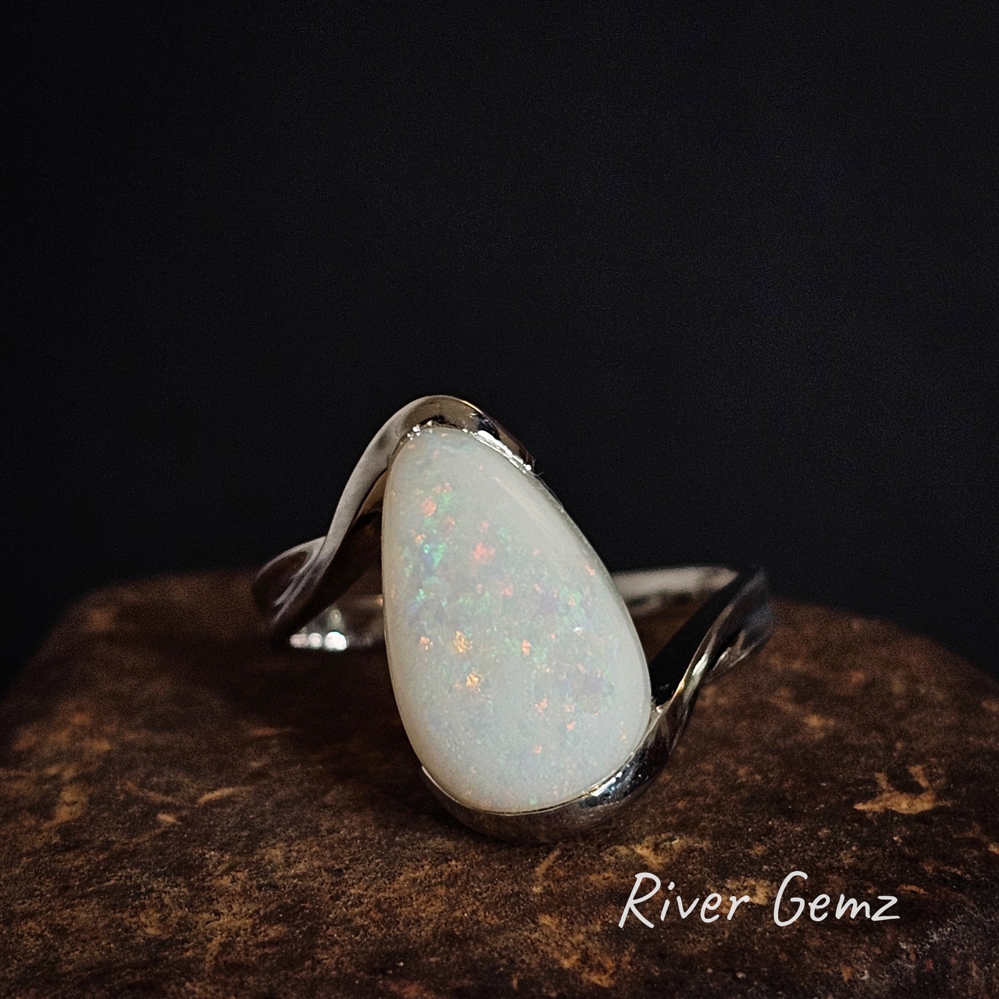Silver ring with a multi-coloured large teardrop-shaped white opal on a dark background, branded 'River Gemz'.