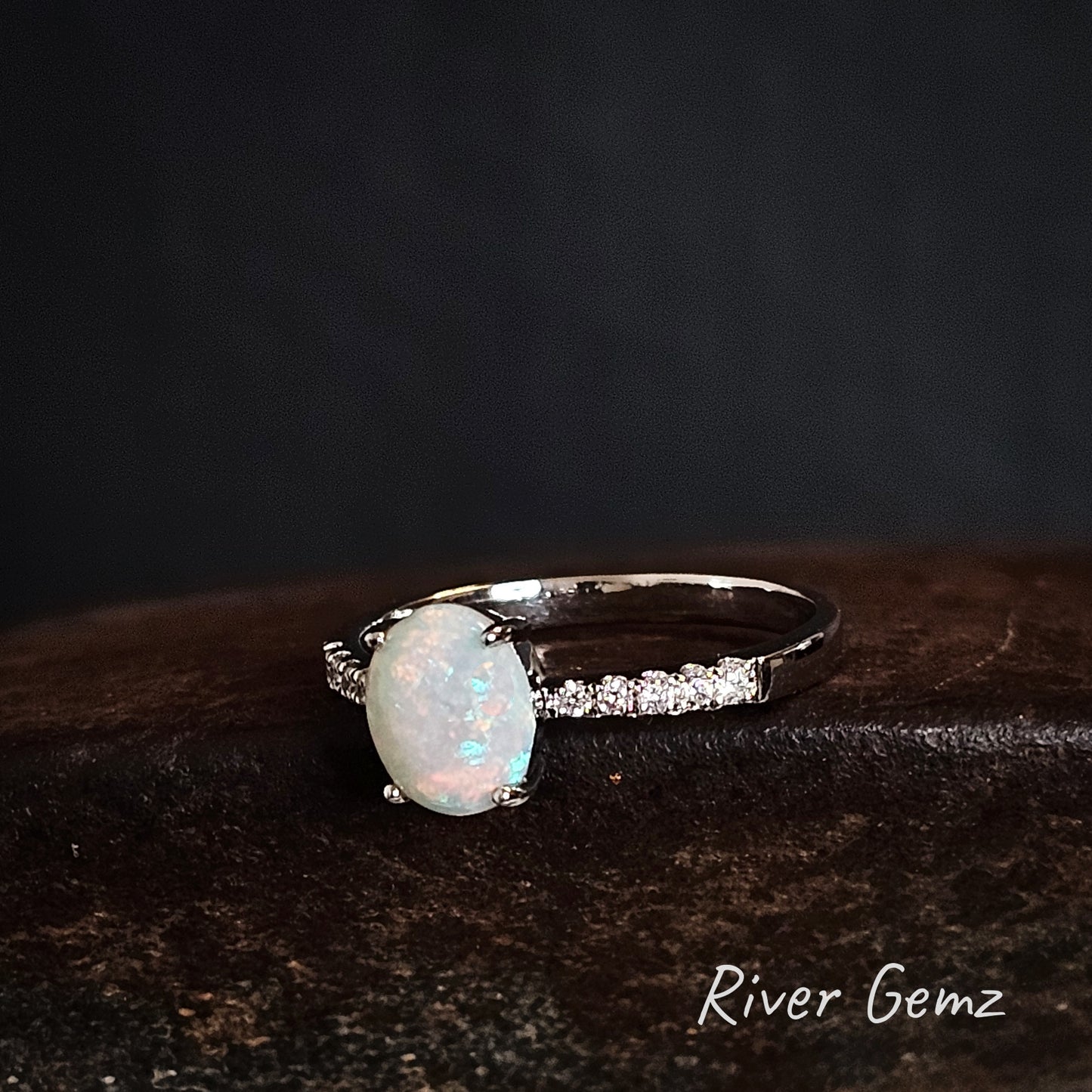 Oval shaped white opal and topaz stones in a silver ring on a dark background, branded 'River Gemz'.