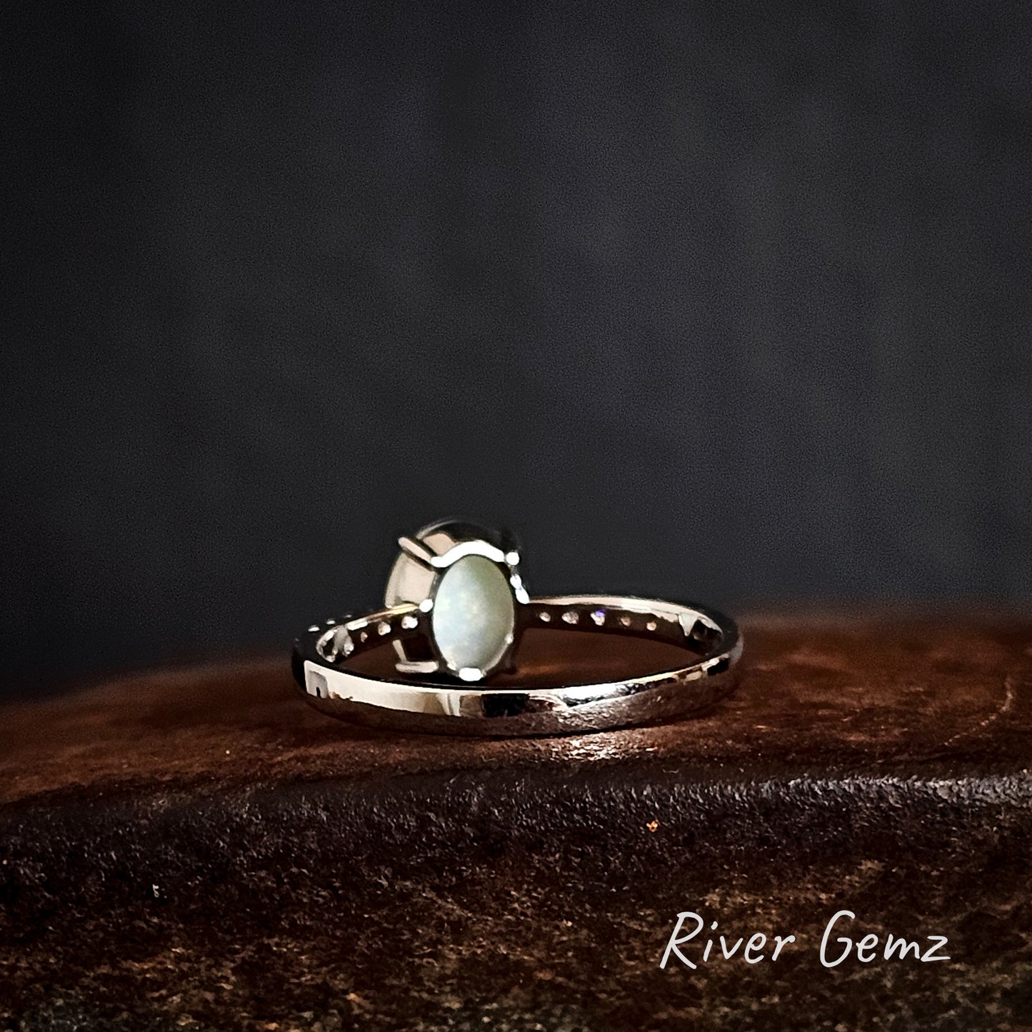 Back of silver ring shows the white base of the opal on a dark brown surface, branded 'River Gemz'.