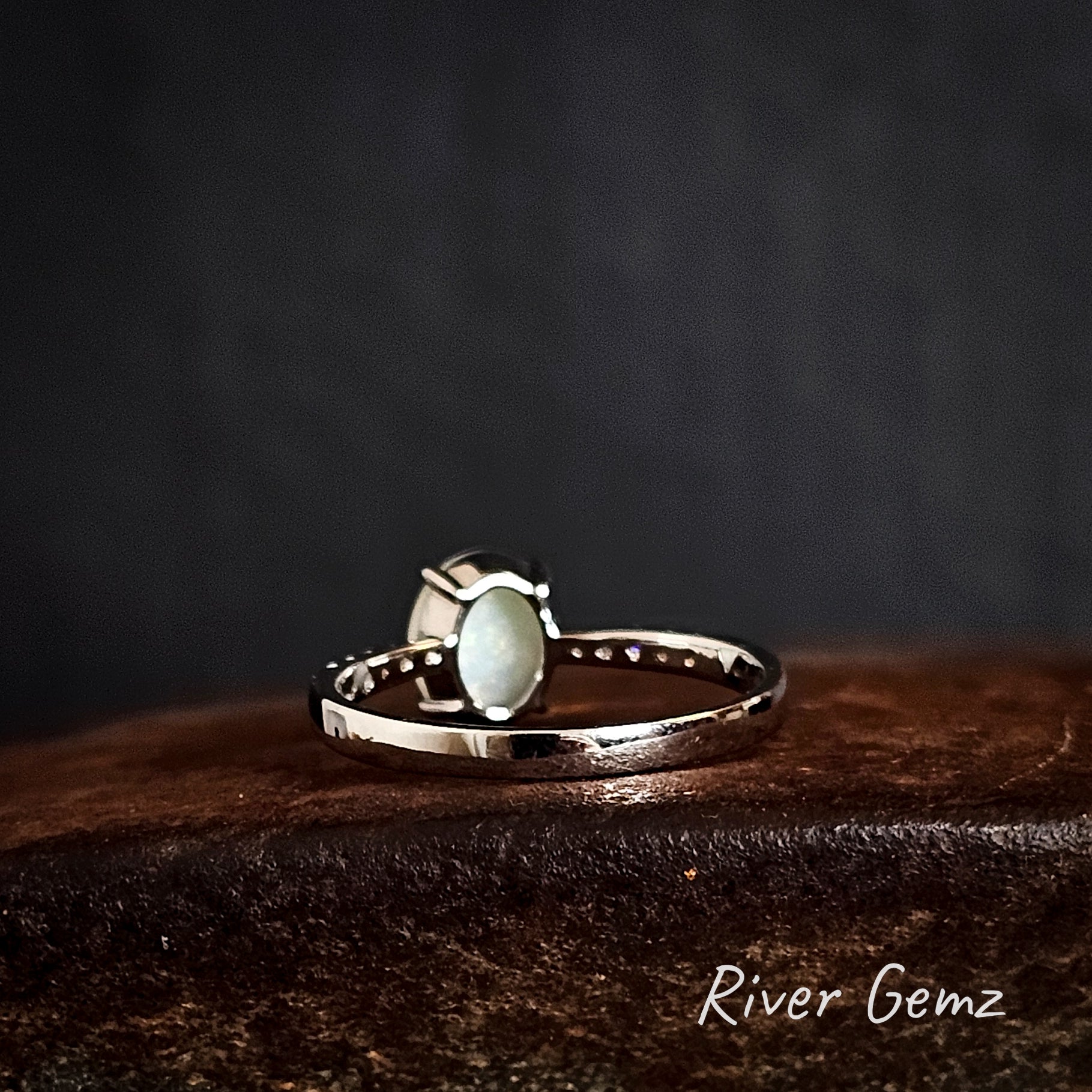 Back of silver ring shows the white base of the opal on a dark brown surface, branded 'River Gemz'.