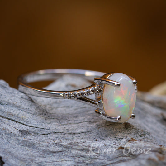 Oval shaped white opal with small white topaz stones in silver ring laying on light grey textured wood.