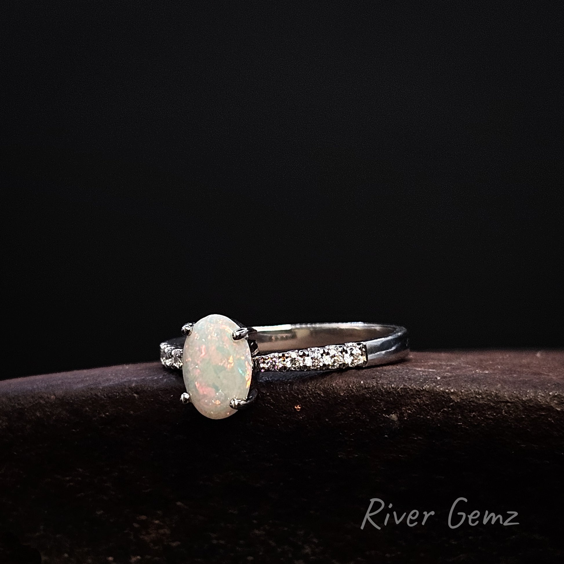 White opal ring with white topaz shoulders on a dark background, branded 'River Gemz'.