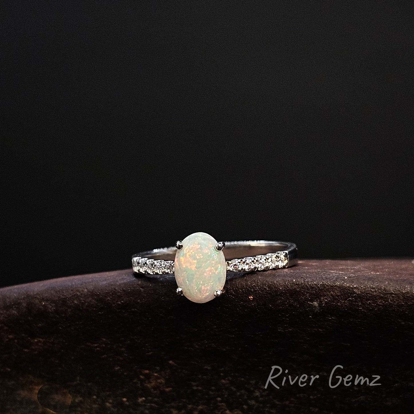 Ring with an opal stone on a dark background, branded 'River Gemz'.