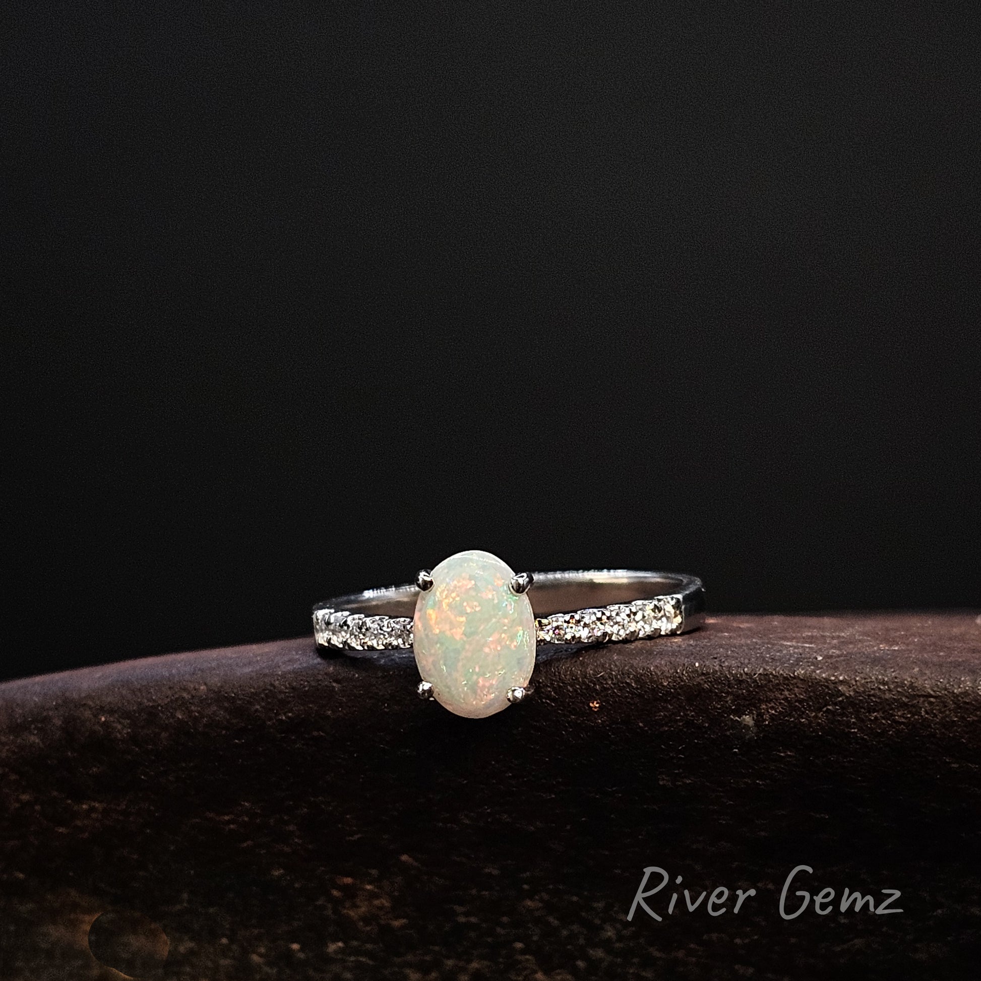Ring with an opal stone on a dark background, branded 'River Gemz'.