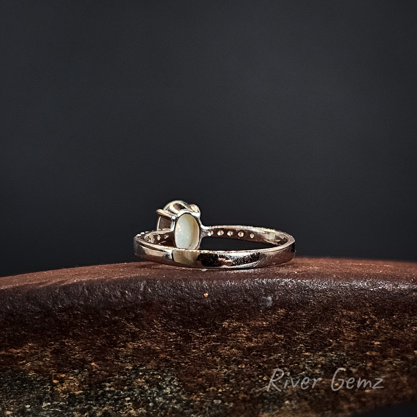 Back of silver ring showing the light base tone of the white opal on a dark surface, branded 'River Gemz'.
