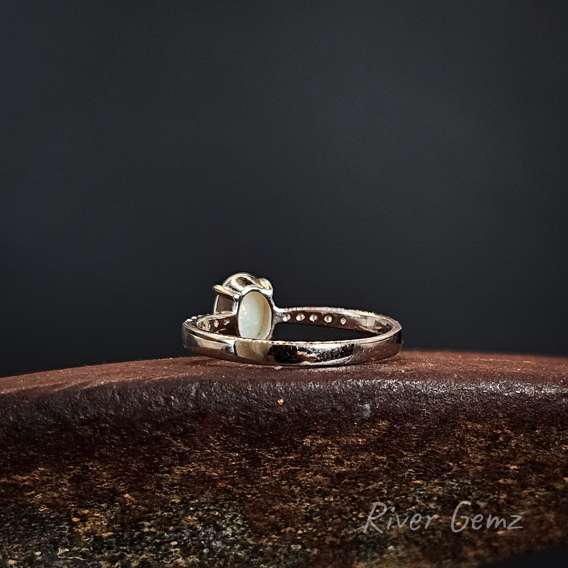 Back of silver ring showing the light base tone of the white opal on a dark surface, branded 'River Gemz'.