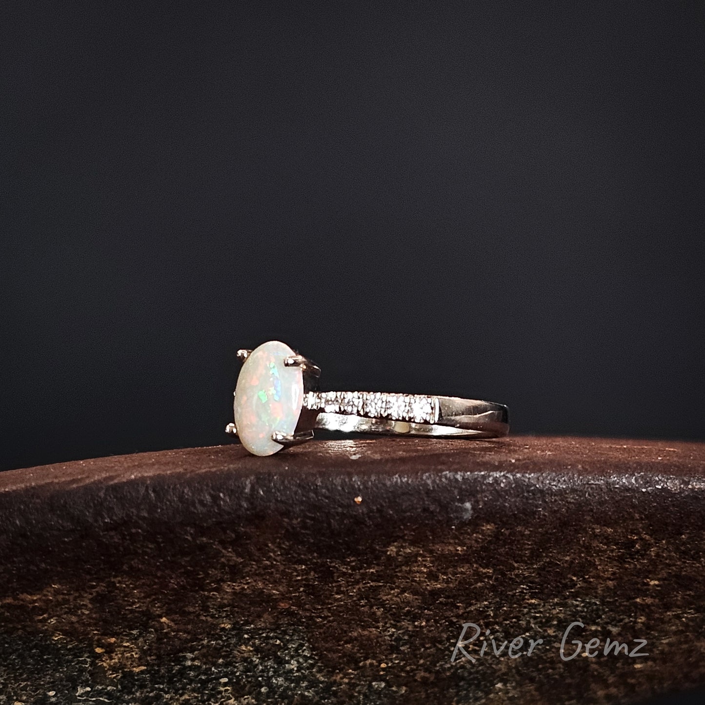 Opal ring with white topaz accents on a dark background, featuring 'River Gemz' branding.