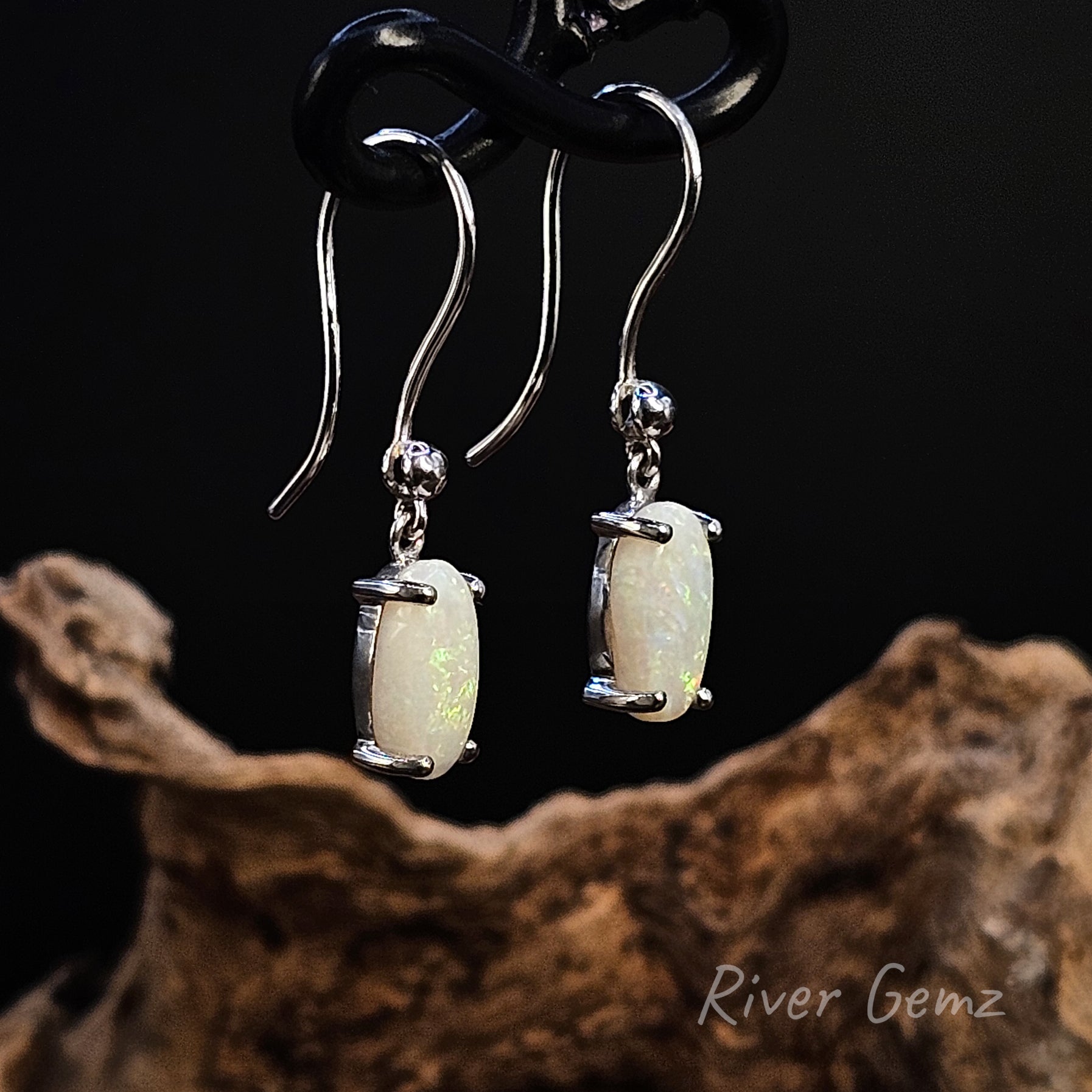 White opals claw set in shepherd hooks on a dark background with 'River Gemz' branding.