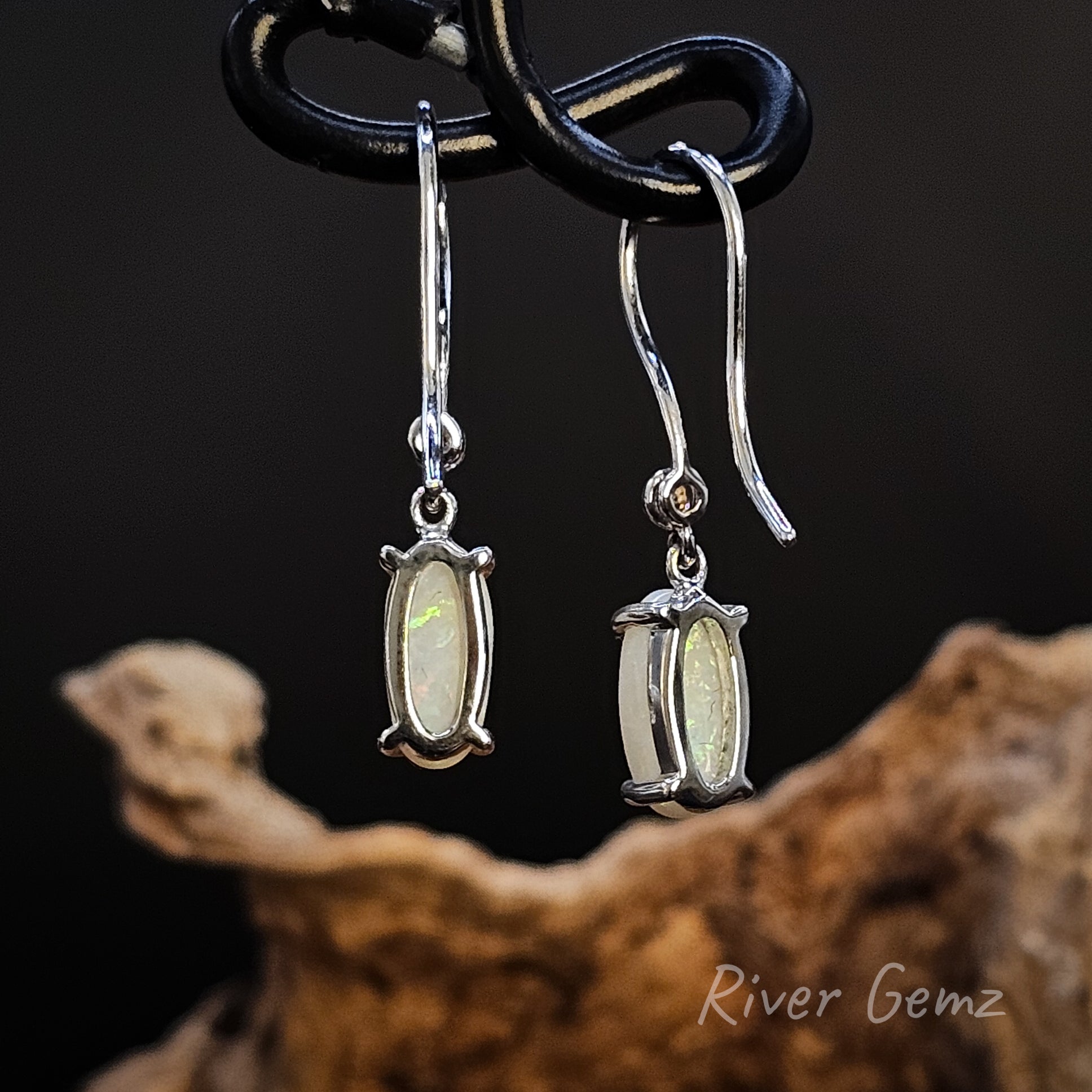 Rear view of pair of silver earrings showing solid opal stones on a dark background