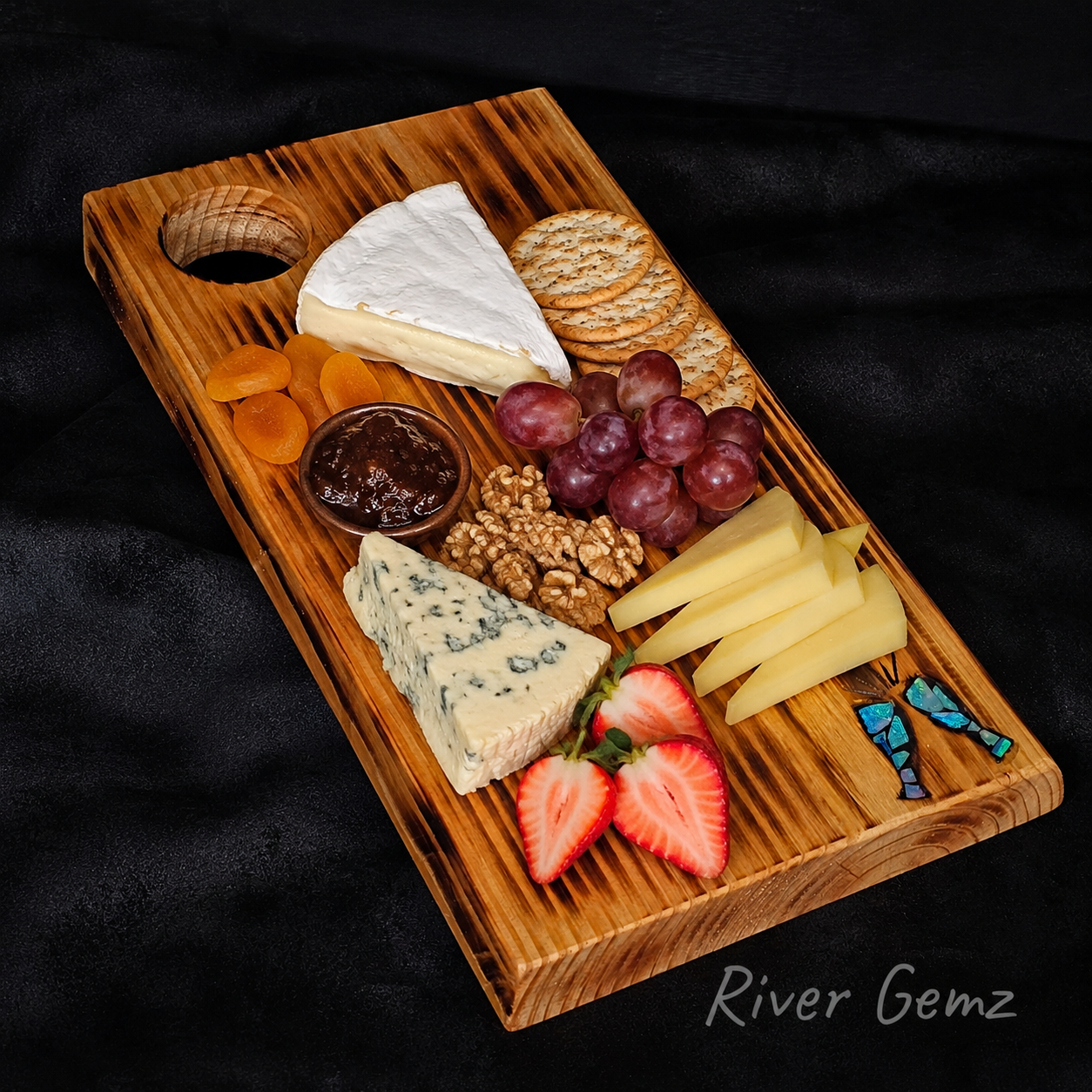 Wooden cheese board with assorted cheeses, fruits, and nuts on a black background.