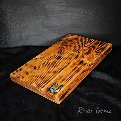 Wooden cutting board with a torched surface on a dark background, featuring the brand 'River Gemz'.