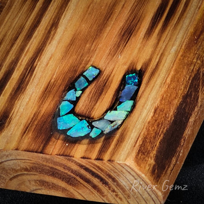 Horseshoe-shaped motif with blue opals inlayed in a wooden surface, branded 'River Gemz'.